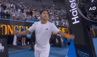 Man In White Shirt Holding Tennis Racquet In Front Of Haier Banner GIF