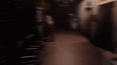 Man In White Shirt In Dark Hallway With Elevator Sign GIF