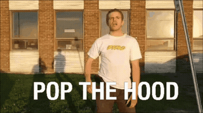 Man In White Shirt In Front Of Brick Building Saying Pop The Hood GIF