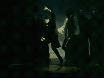 Man In White Shirt In Front Of People In Black Hoods GIF