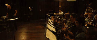 Man In White Shirt Kneeling Playing Drums In Dark Room GIF