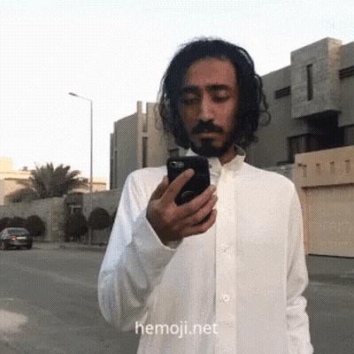 Man In White Shirt Looking At Phone With Hemoji.net GIF