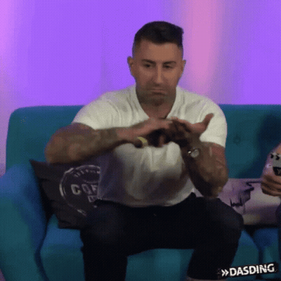 Man In White Shirt Making Heart Shape On Blue Couch GIF