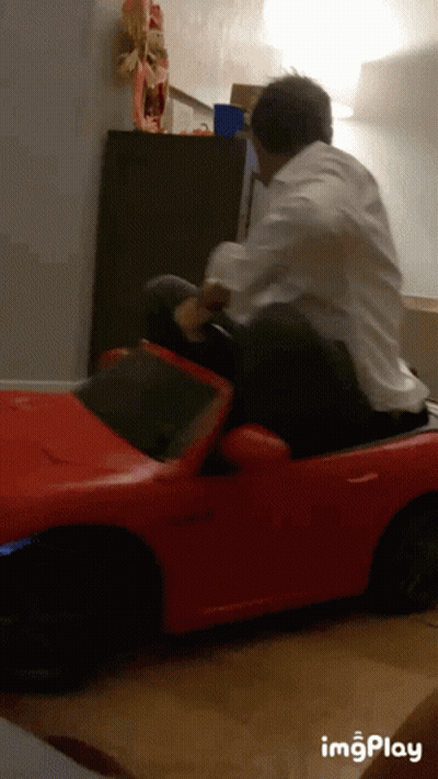 Man In White Shirt Riding Red Toy Car GIF