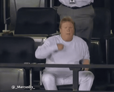 Man In White Shirt Sitting In Stadium With Fist In Air GIF