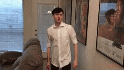 Man In White Shirt Standing Next To Couch And Star Wars Poster GIF
