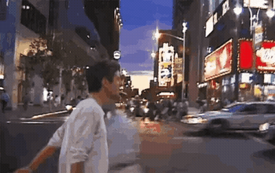 Man In White Shirt Walking Down Busy City Street At Night GIF
