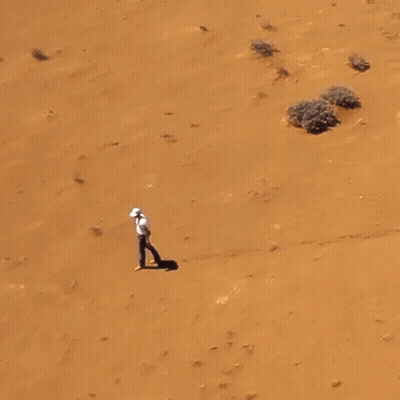 Man In White Shirt Walking In Sandy Desert GIF