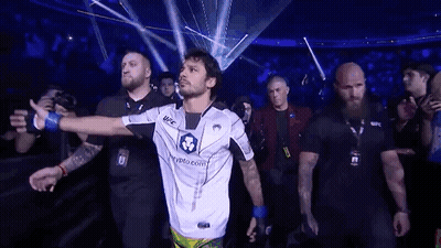 Man In White Shirt Walking Through Crowd In Dark Room GIF