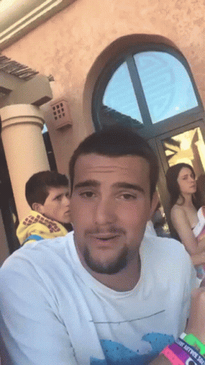 Man In White Shirt With Wave In Front Of Building GIF