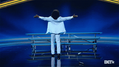 Man In White Suit Arms Outstretched On Stage With BET Logo GIF