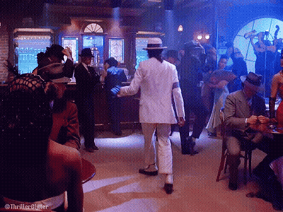 Man In White Suit Dancing In Room With People At Tables GIF