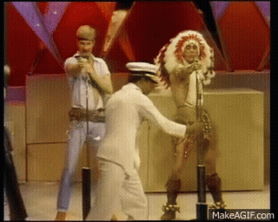 Man In White Suit Dancing With Woman In Native American Costume GIF