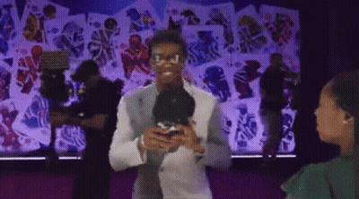 Man In White Suit Holding Microphone Talking To Woman In Green Shirt GIF