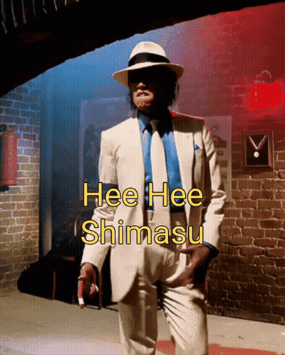 Man In White Suit In Front Of Brick Wall Saying Hee Hee Shimasu GIF