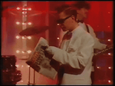 Man In White Suit Playing Guitar And Reading Newspaper GIF