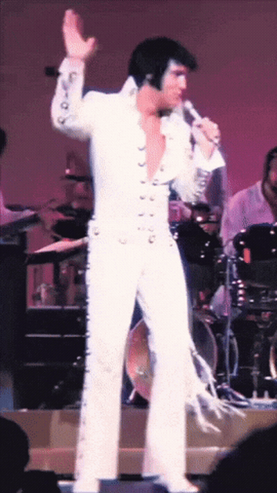Man in White Suit Singing Into Microphone on Stage