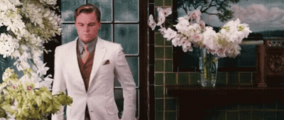 Man In White Suit Standing By Window With Flowers GIF