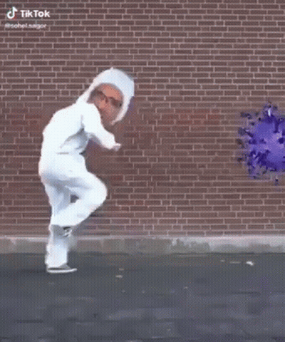Man In White Suit Walking In Front Of Brick Wall With Virus Picture GIF