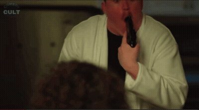 Man In White Sweater Holding Black Object In Mouth Saying Comes Cult GIF