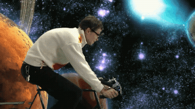 Man In White Sweater Riding Bike In Front Of Planet GIF