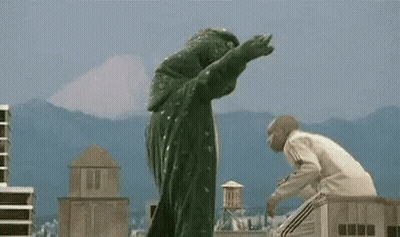 Man In White Sweater Standing Next To Giant Monster GIF