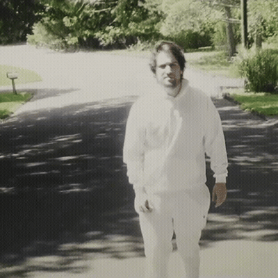 Man In White Sweatshirt And Pants Walking Down Road GIF