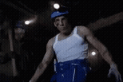 Man In White Tank Top And Blue Shorts Dancing In Dark Room GIF