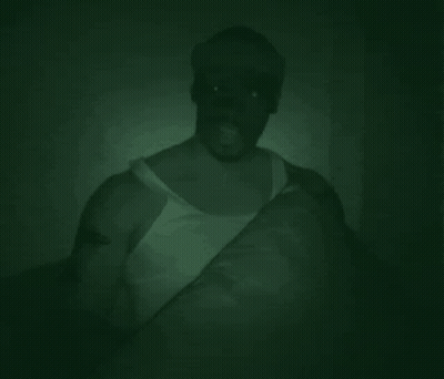 Man In White Tank Top Holding Pillow In Dark Room GIF