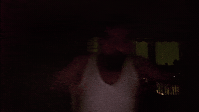 Man In White Tank Top In Front Of This Is Mustafa Sign GIF
