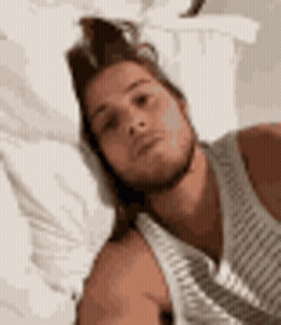 Man In White Tank Top Laying On Bed With Pillow GIF