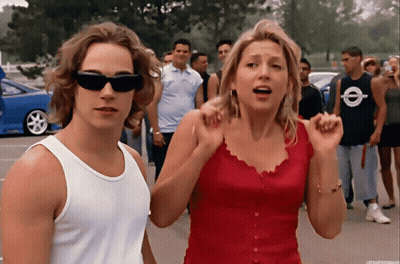 Man In White Tank Top Next To Woman In Red GIF