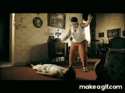 Man In White Tank Top Standing Next To Man Laying On Floor GIF