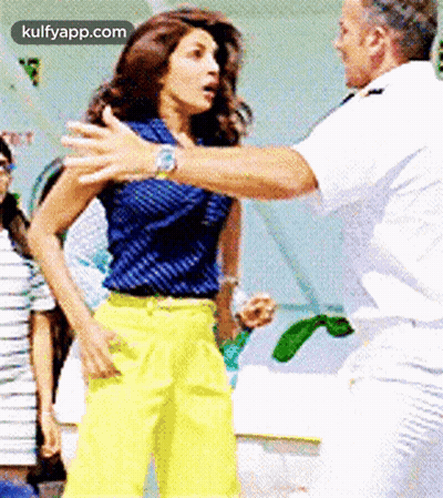 Man In White Uniform Next To Woman In Blue Top And Yellow Pants GIF
