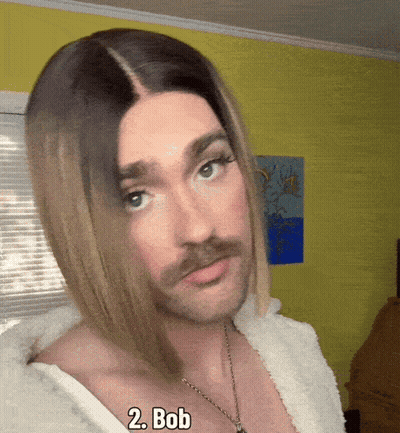 Man In Wig And Necklace With Bob On Chest GIF