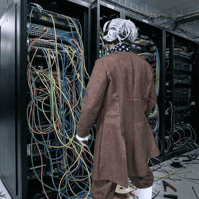 Man In Wig In Front Of Server Rack With Cables GIF
