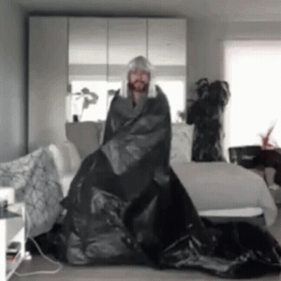 Man In Wig Wrapped In Black Bag In Living Room GIF