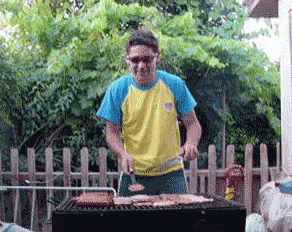 Man In Yellow And Blue Shirt Grilling Meat GIF