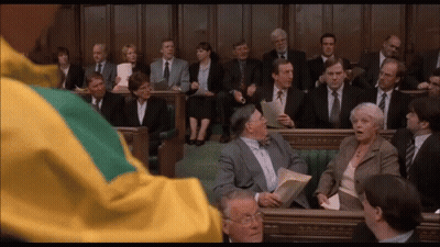 Man In Yellow And Green Jacket With People In Suits GIF