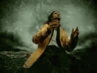 Man In Yellow Coat Sitting On Rock GIF