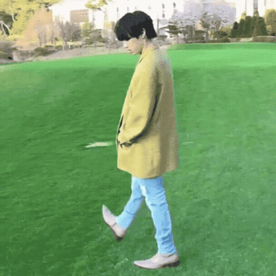 Man In Yellow Coat Walking Across Green Field GIF