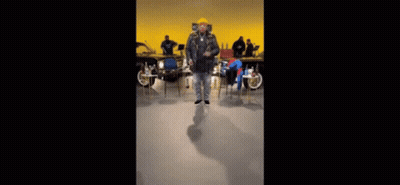 Man In Yellow Hat Dancing Among Chairs GIF
