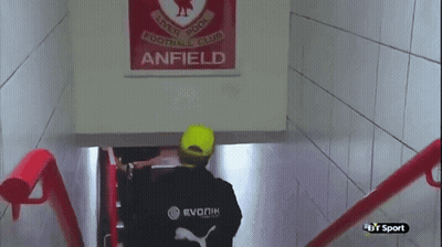 Man In Yellow Hat Walking Down Stairs In Front Of Anfield Sign GIF