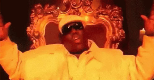 Man In Yellow Jacket And Hat Sitting With Arms In Air GIF