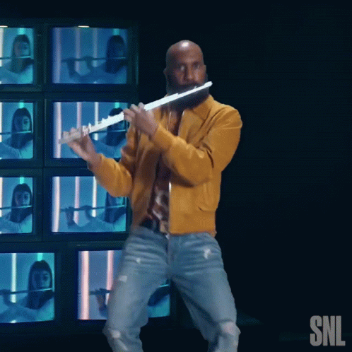 Man in Yellow Jacket Playing Flute in Front of SNL Logo