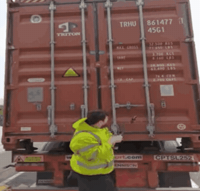 Man In Yellow Jacket Pointing At Red Triton Container GIF