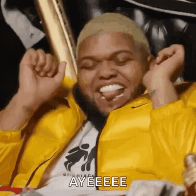 Man In Yellow Jacket Sitting In Chair With Trophies GIF