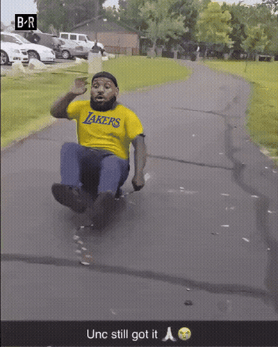 Man In Yellow Lakers Shirt Sliding Down Road GIF