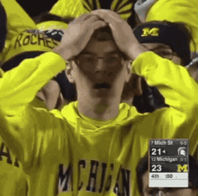 Man In Yellow Michigan Shirt Holding Head In Hands GIF