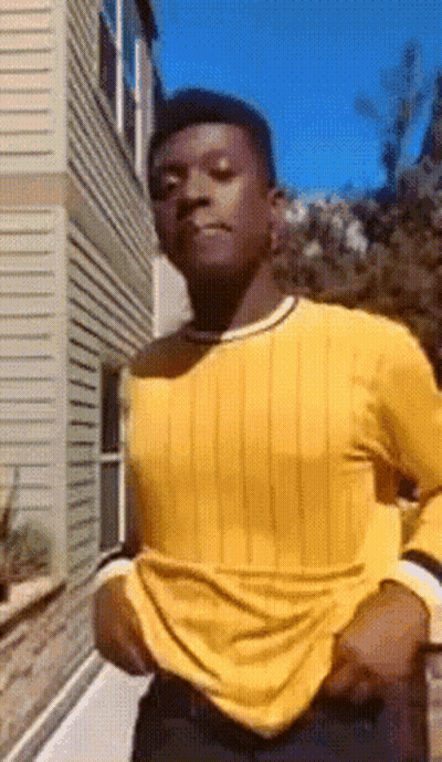 Man In Yellow Shirt And Black Pants Standing In Front Of Building GIF